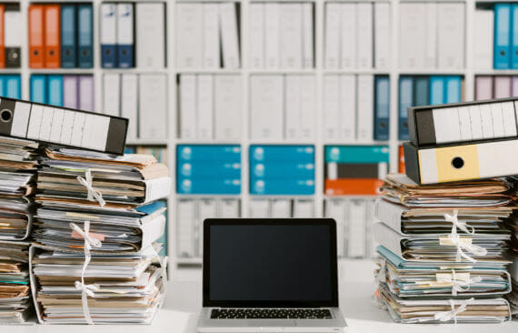 Piles of paperwork in the office and laptop on the desktop