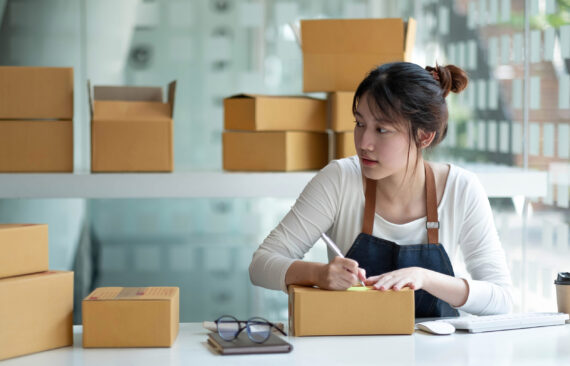 Woman packing and labeling shipping boxes for a small business order at a home workspace