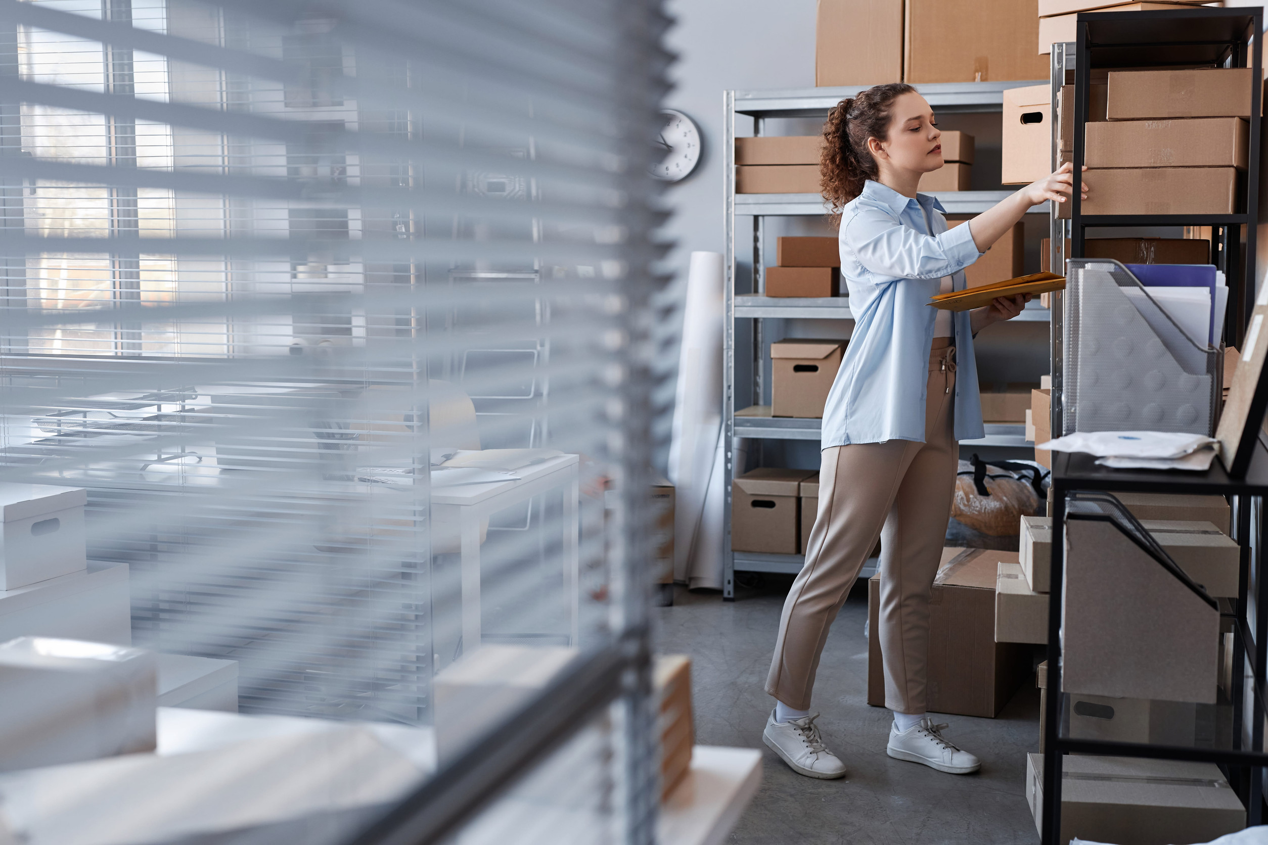 Employee organizing office storage shelves with labeled boxes and files in an organized workspace.