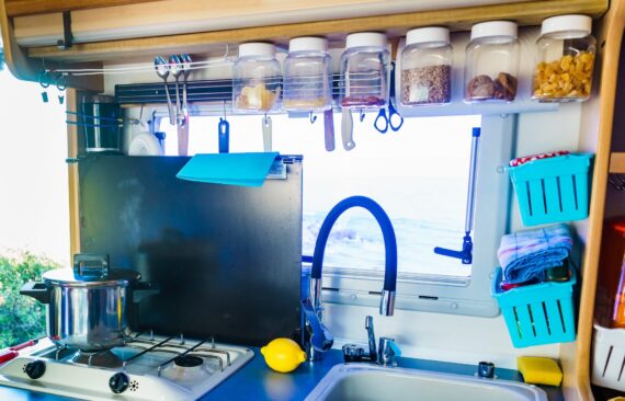 Space-saving storage ideas in an organized RV kitchen, featuring hanging utensils, clear pantry containers, and wall-mounted organizers.