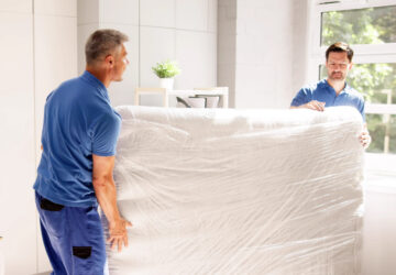 Deux déménageurs transportant un matelas enveloppé dans du plastique pour l’entreposage